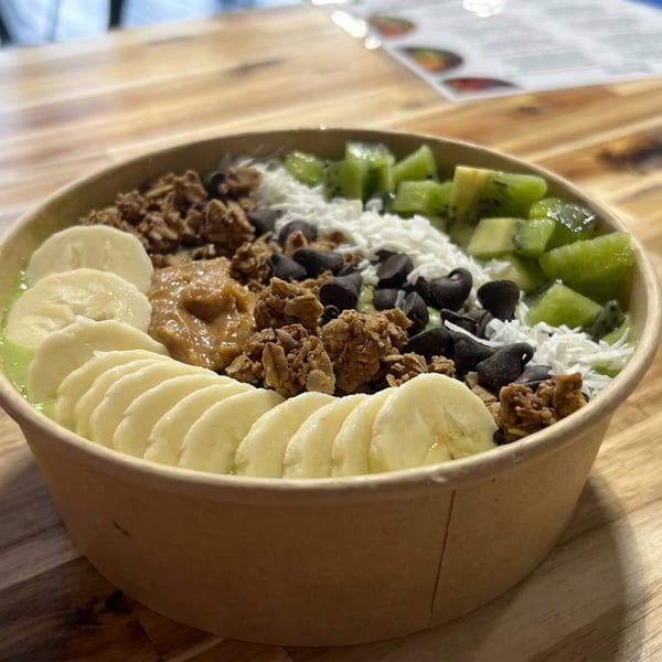 Acai bowl topped with sliced banana, kiwi, coconut, black beans, granola, and nut butter on a wooden table.