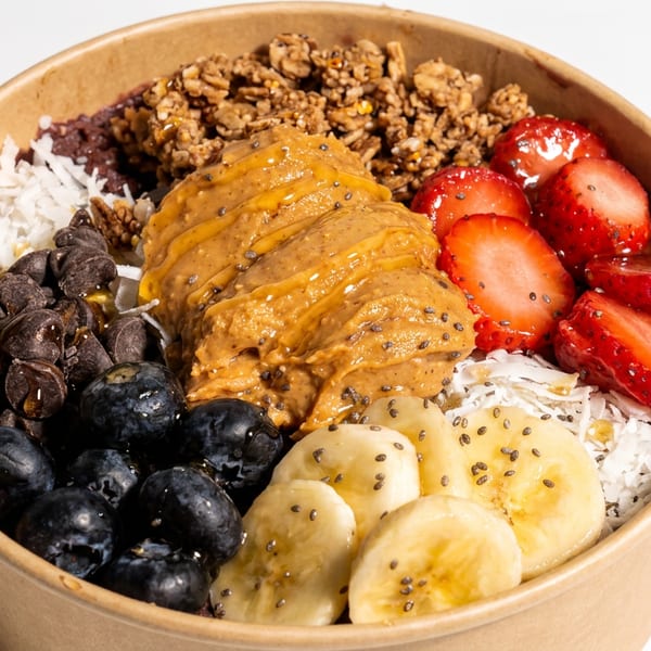 Açaí bowl topped with peanut butter, granola, strawberries, banana, blueberries, chocolate chips, coconut, and chia seeds.