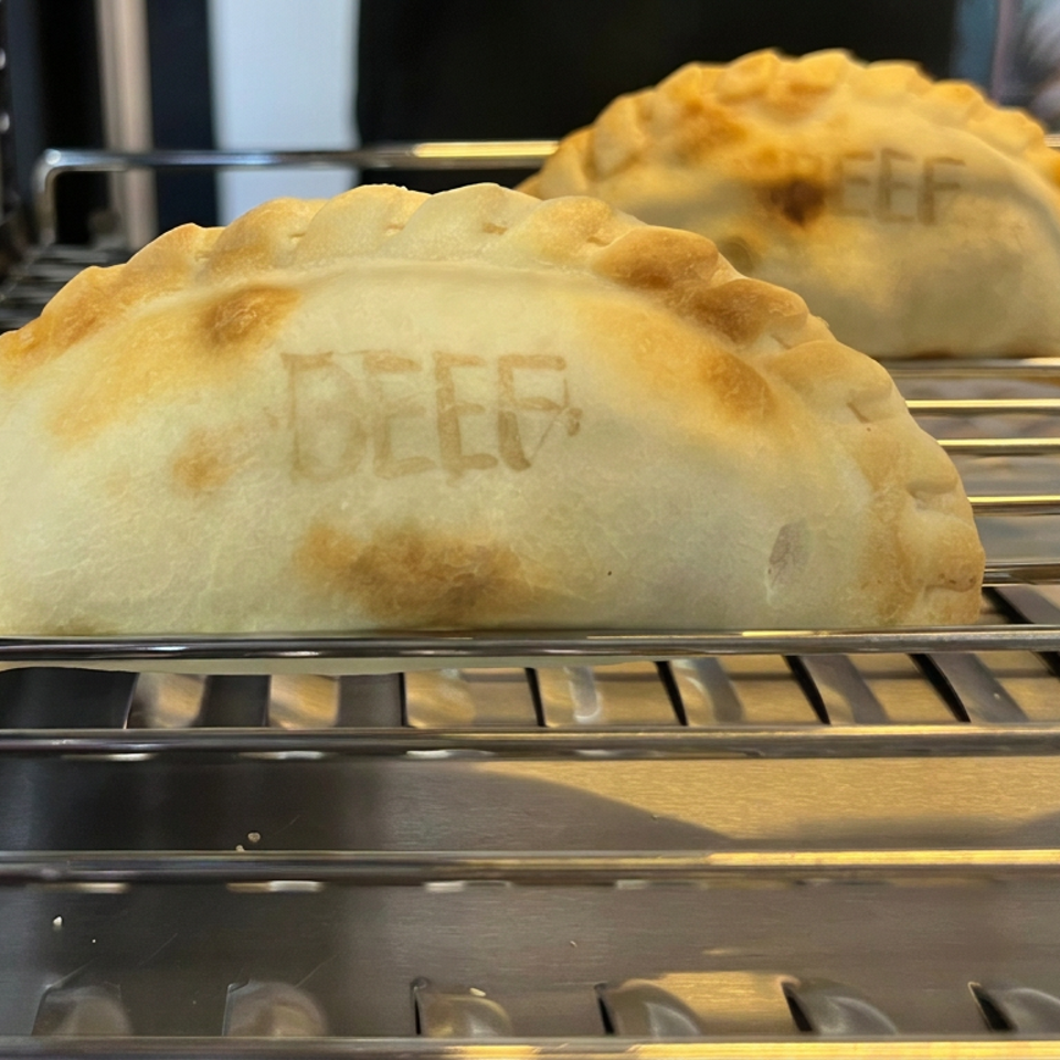 Golden-brown baked empanadas displayed on metal cooling racks in a bakery case.