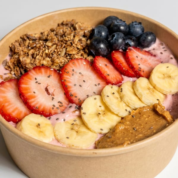 Pink smoothie bowl topped with granola, blueberries, sliced strawberries, bananas, chia seeds, and peanut butter.