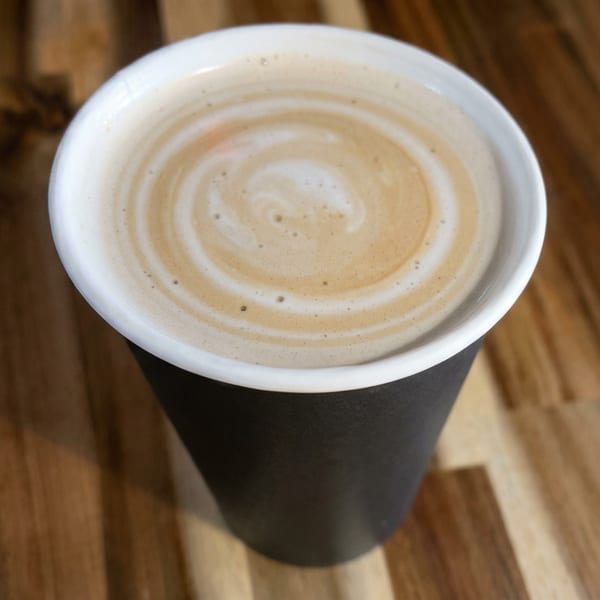 Foamy coffee in a black cup on a rustic wooden table.