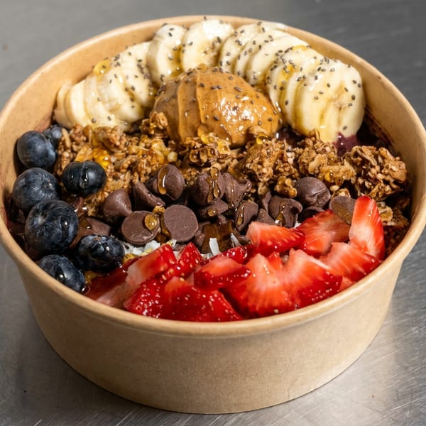 Fruit-topped smoothie bowl with banana, blueberries, strawberries, granola, chocolate chips, peanut butter, and chia seeds.