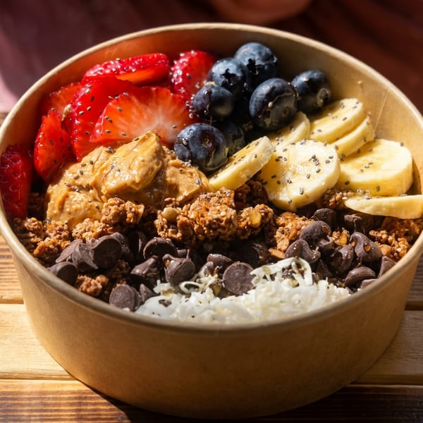 Fruit and granola bowl topped with strawberries, blueberries, banana, peanut butter, chocolate chips, coconut, and chia seeds.